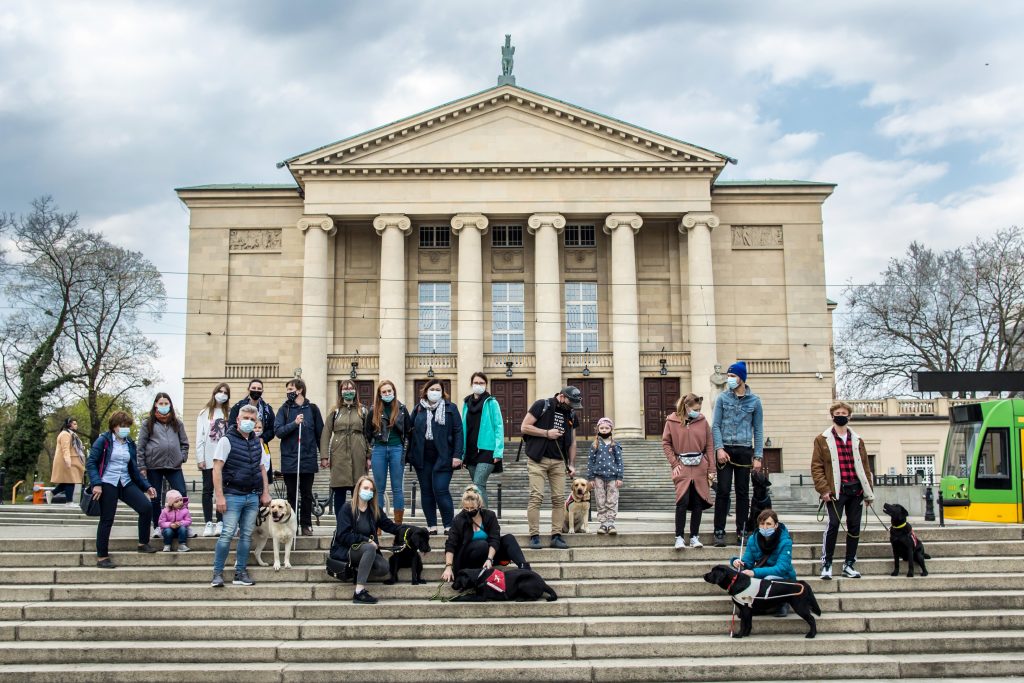 puppy raisers and their dogs on the steps in front of a building